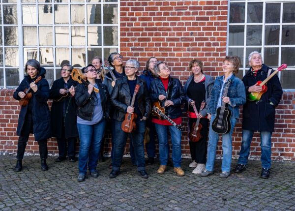 Gruppe von elf Personen steht vor einer Klinkermauer mit Ukulelen in der Hand