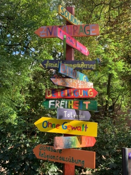 Wegweiser mit verschiedenen bunt gemalten Schildern auf denen Begriffe wie Solidarität, Beteiligung oder Freiheit gemalt sind