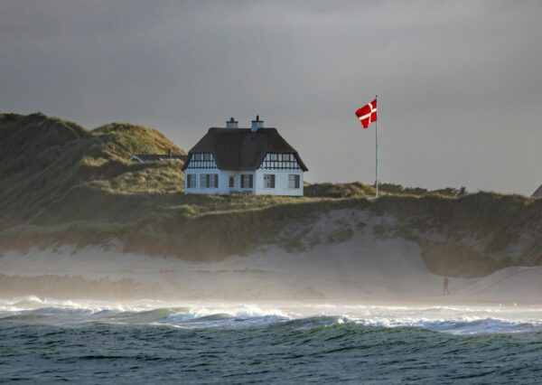 Ein Reetdachhaus mit einer dänischen Flagge an einer Küstenklippe mit Meer und Dünen