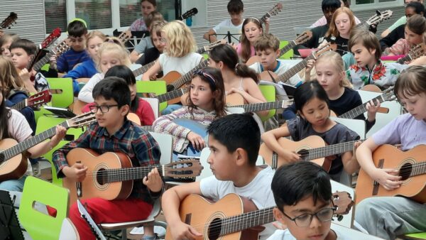 Foto zahlreicher Kinder, die Gitarre spielen in sommerlicher Atmosphäre