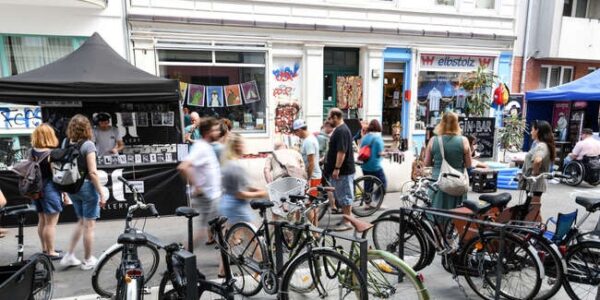 Straßenszenerie in Altona mit Blick auf ein Ladengeschäft, einen Essensstand, Passant*innen und Fahrradständern